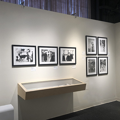 A white wall with seven black-and-white images and a display case hanging from the wall.