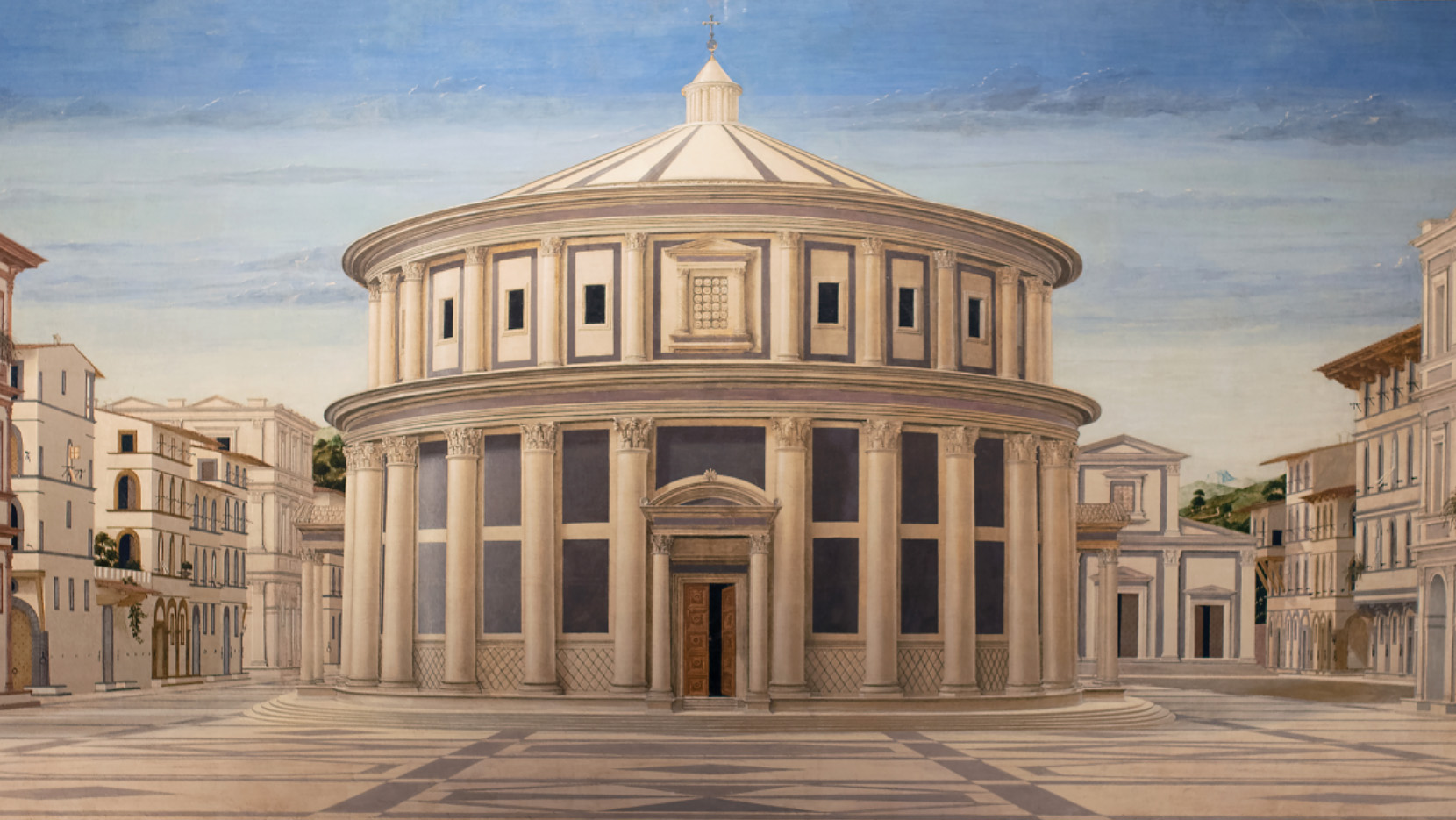 An illustration of the Palazzo Ducale in Urbino. The two-story-tall building is white and grey, and is round in shape with the roof meeting in the center to become a small tower. The building is split horizontally into two sections. The bottom section has step leading to a large door with a rounded overhang and large, ornate columns holding up an overhang that goes around the building's circumference. There are two more doors about ninety degrees from the center door. The top section is inset from the overhang and isn't as tall as the bottom section. It has shorter columns, with a false door parallel to the front door. Windows are in the center of the wall on either side of the columns, and repeat on the building's circumference. The Palazzo is in the middle of an open square, and regular buildings of a similar color are perpendicular to it. The sky is blue with white clouds, and trees can be seen in the distance.
