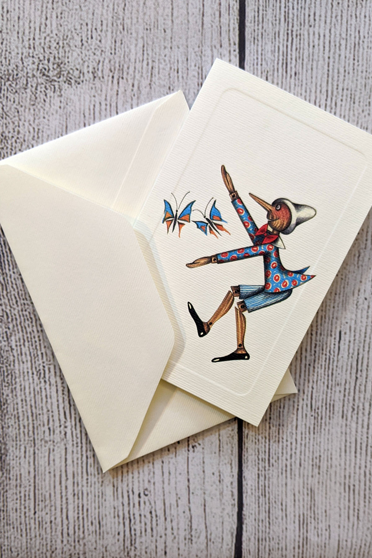 A card featuring and illustration of Pinocchio playing with butterflies on the front.